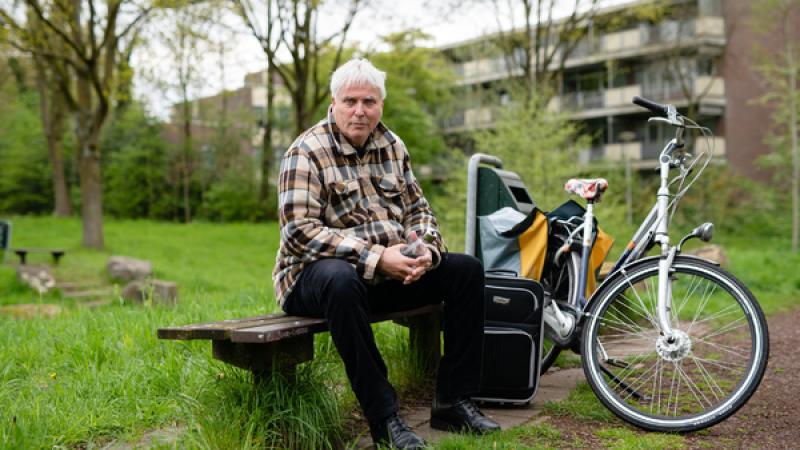 man zit op bankje met naast hem zijn fiets met fietstas